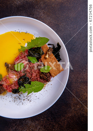 A beef tartar on a white plate against a dark background. Master class in the kitchen. The process A beef tartar on a white plate against a dark background. Master class in the kitchen. The process 67234766