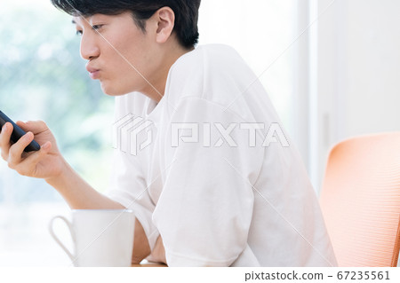 一個年輕的男人,一邊看著智能手機說話 一個年輕的男人,一邊看著智能手機說話 67235561
