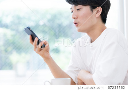 A young man talking while watching a smartphone A young man talking while watching a smartphone 67235562