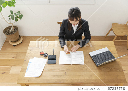 Woman in business suit imprinting documents at desk Woman in business suit imprinting documents at desk 67237758