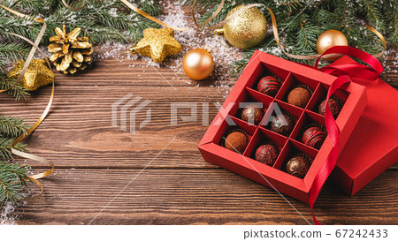 Chocolate candies in a red craft box wooden Christmas background fir branches of a New Year's toy. Flat layout top view. Chocolate candies in a red craft box wooden Christmas background fir branches of a New Year's toy. Flat layout top view. 67242433