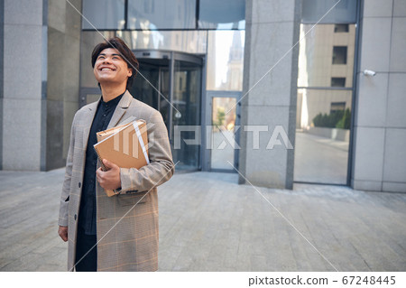 Cheerful young man with documents standing on the street Cheerful young man with documents standing on the street 67248445