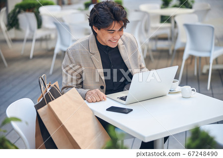 Cheerful young man using notebook in outdoor cafe Cheerful young man using notebook in outdoor cafe 67248490