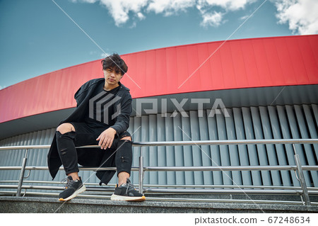 Handsome young man sitting on handrail on the street Handsome young man sitting on handrail on the street 67248634