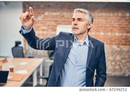 Adult businessman is standing in his modern office Adult businessman is standing in his modern office 67249252