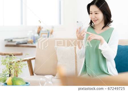 在客廳裡操作智能手機的中年女人 在客廳裡操作智能手機的中年女人 67249725