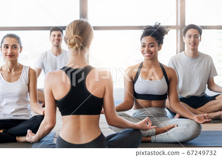 Young sporty people practicing yoga with instructor, making easy sit pose Young sporty people practicing yoga with instructor, making easy sit pose 67249732