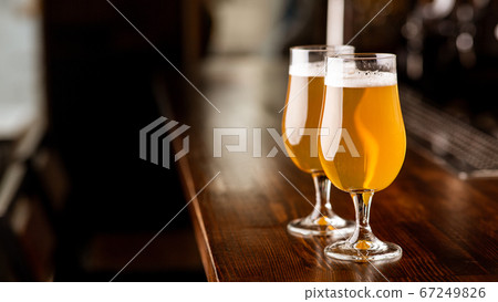 Service at pub. Glasses with beer in light on wooden bar counter Service at pub. Glasses with beer in light on wooden bar counter 67249826