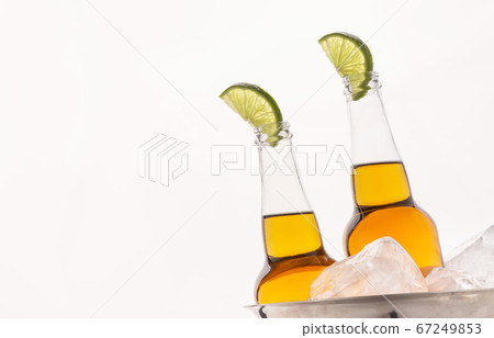 Cold drink. Transparent beer bottles with light ale and slice of lime in metal bucket with ice Cold drink. Transparent beer bottles with light ale and slice of lime in metal bucket with ice 67249853