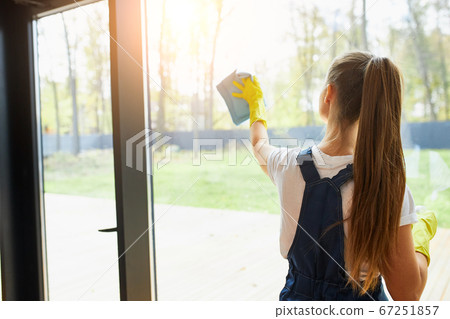 Rear view on young cleaner lady washing glass of window Rear view on young cleaner lady washing glass of window 67251857