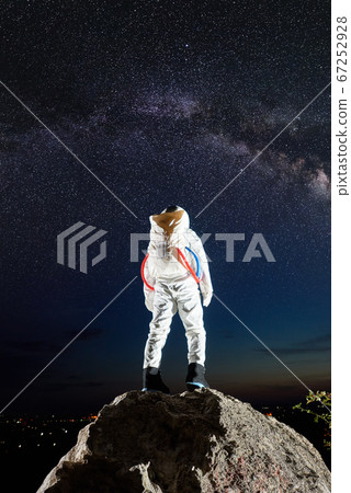Astronaut standing on rocky mountain under starry sky. 67252928