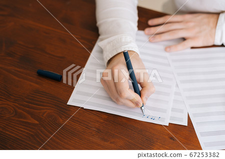 Close-up of hands of unrecognizable man writing musical notes with pencil on sheet music Close-up of hands of unrecognizable man writing musical notes with pencil on sheet music 67253382