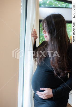 Pretty young pregnant woman standing by the window Pretty young pregnant woman standing by the window 67255400