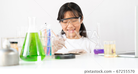 Adorable school girl writing a scientific result while doing a scientific. 67255570