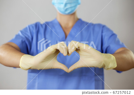 Doctor in a face mask and gloves forming a heart in front of blue shirt, 67257012