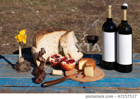 wine tasting outdoors. wine glass and bottle with blank etiquette for mockup, cheese, bread and tomatoes snacks on a haystack. 67257517