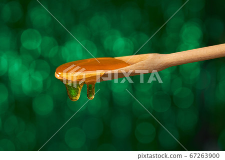 Sweet honey poured from a wooden spoon, on a green Sweet honey poured from a wooden spoon, on a green 67263900