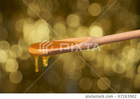Sweet honey poured from a wooden spoon, on a gold 67263902