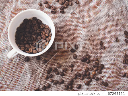 Coffee beans and a white cup on brown rustic raw sackcloth fabric photo. A4 A5 A3 international paper slide poster card with free blank copy space for text. 67265131