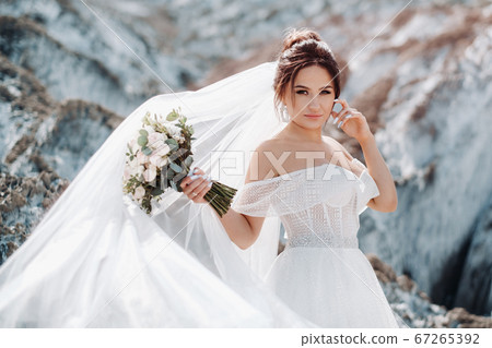 Beautiful bride in a wedding dress with a bouquet on the top of the salt mountains. A stunning young bride with curly hair . Wedding day. . Beautiful portrait of the bride without the groom. 67265392
