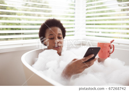Woman with coffee cup using smartphone in a bathtub Woman with coffee cup using smartphone in a bathtub 67268742
