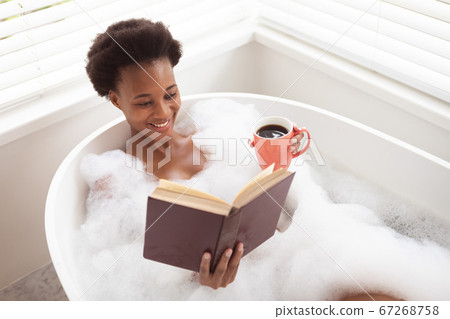Woman with coffee cup reading book in a bathtub Woman with coffee cup reading book in a bathtub 67268758
