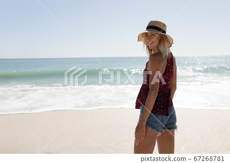 Woman wearing hat smiling while standing on the beach Woman wearing hat smiling while standing on the beach 67268781