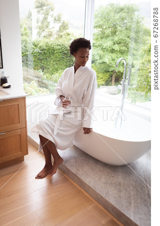 Woman with glass sitting on bathtub Woman with glass sitting on bathtub 67268788