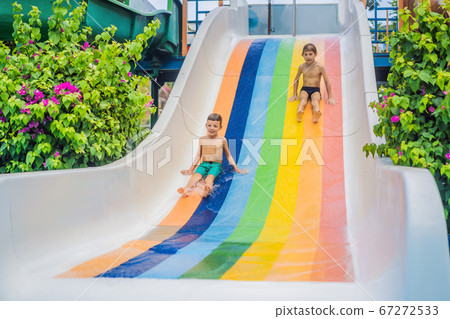 Young boy or kid has fun splashing into pool after going down water slide during summer 67272533