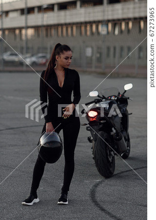 A beautiful biker girl holding helmet next superbike outside a building. 67273965