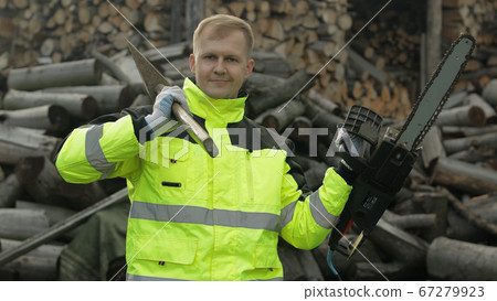Lumberjack worker. Man woodcutter holds big axe and electric chainsaw in his hands. Firewood Lumberjack worker. Man woodcutter holds big axe and electric chainsaw in his hands. Firewood 67279923