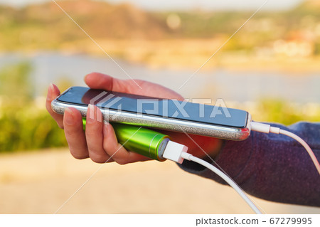 A girl uses a smartphone outdoors while charging A girl uses a smartphone outdoors while charging 67279995