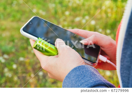 A girl uses a smartphone outdoors while charging A girl uses a smartphone outdoors while charging 67279996