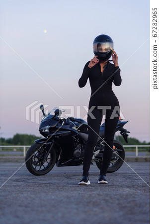Biker woman in black leather jacket and full face helmet sits near stylish sports motorcycle at urban parking. Traveling and active lifestyle concept. Biker woman in black leather jacket and full face helmet sits near stylish sports motorcycle at urban parking. Traveling and active lifestyle concept. 67282965