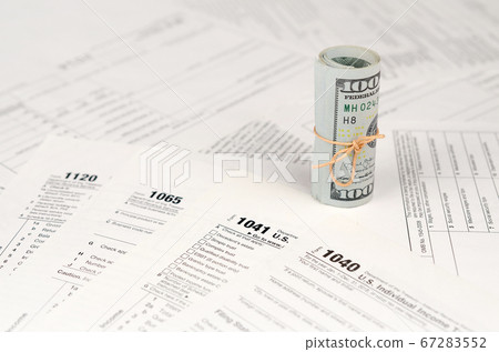 Tax forms lies near roll of hundred dollar bills. Tax forms lies near roll of hundred dollar bills. 67283552