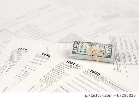 Tax forms lies near roll of hundred dollar bills. 67283826