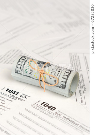 Tax forms lies near roll of hundred dollar bills. 67283830