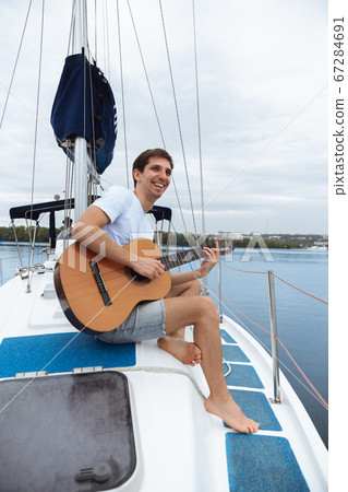 Young cheerful man playing guitar at boat party outdoor, smiling and happy Young cheerful man playing guitar at boat party outdoor, smiling and happy 67284691