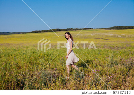 Beautiful woman in dress walks on the field with yellow flowers Beautiful woman in dress walks on the field with yellow flowers 67287113