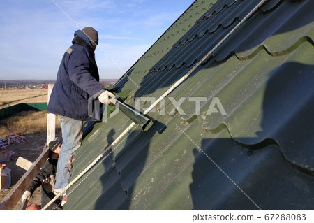 Installation of the roof of the house is done by a worker, snow guards and other roof elements. Installation of the roof of the house is done by a worker, snow guards and other roof elements. 67288083