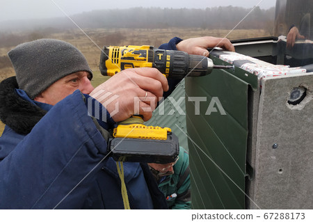 A worker on the roof of the house sheathes the chimney with a metal profile 67288173
