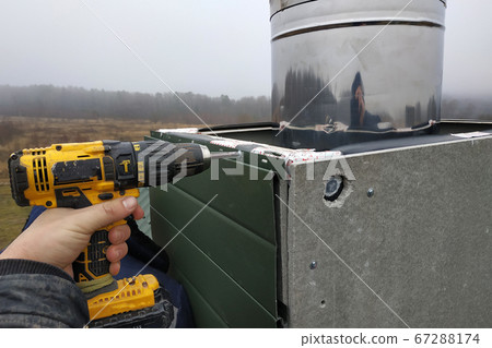 A worker on the roof of the house sheathes the chimney with a metal profile 67288174