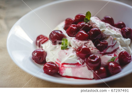 Cottage cheese cream and cream dessert with cherries and mint for breakfast on a white plate on a 67297491