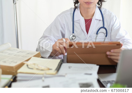 Asian doctor researching reading medical books and online knowledge to find treatment patient guidelines In the doctor's room office Asian doctor researching reading medical books and online knowledge to find treatment patient guidelines In the doctor's room office 67300817