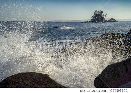 A small fishing boat passes over the breaking waves 67304521