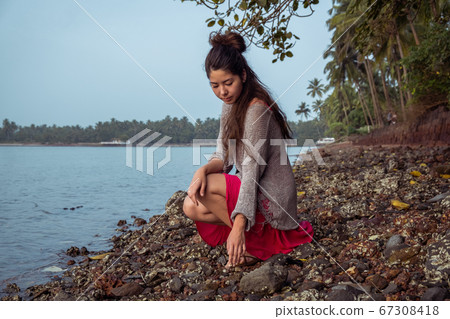 Girl with dreadlocks sits on a rocky beach Girl with dreadlocks sits on a rocky beach 67308418