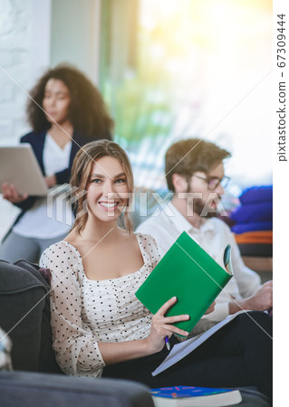 Girl with book looking at camera, friends at distance busy Girl with book looking at camera, friends at distance busy 67309444