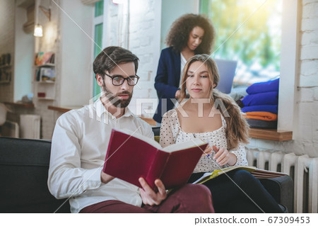 Bearded guy reading book and two girls. 67309453