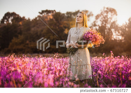 Young woman with a bouquet of wildflowers standing on a sunny blooming meadow Young woman with a bouquet of wildflowers standing on a sunny blooming meadow 67310727