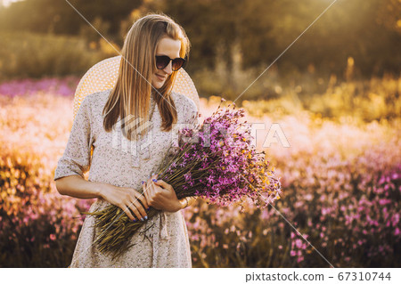 Young woman with a bouquet of wildflowers standing on a sunny blooming meadow Young woman with a bouquet of wildflowers standing on a sunny blooming meadow 67310744